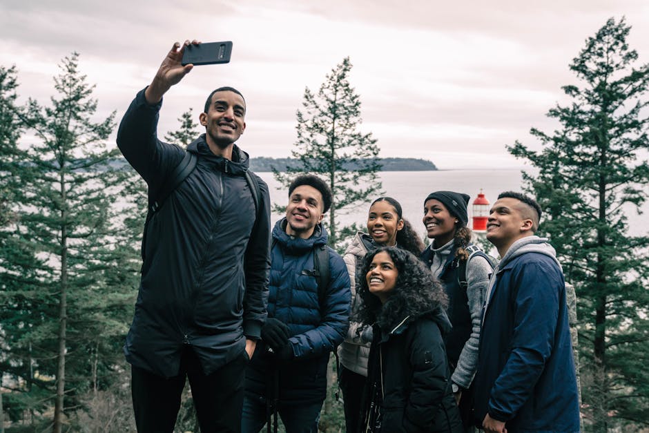 A diverse group of friends enjoying a hiking adventure and taking a selfie outdoors near a scenic lighthouse.