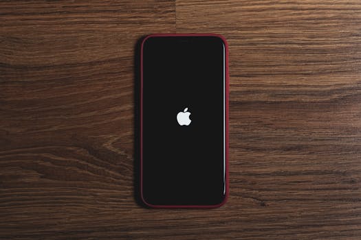 Minimalist flat lay of a smartphone with Apple logo on a wooden surface, ideal for tech and gadget themes.