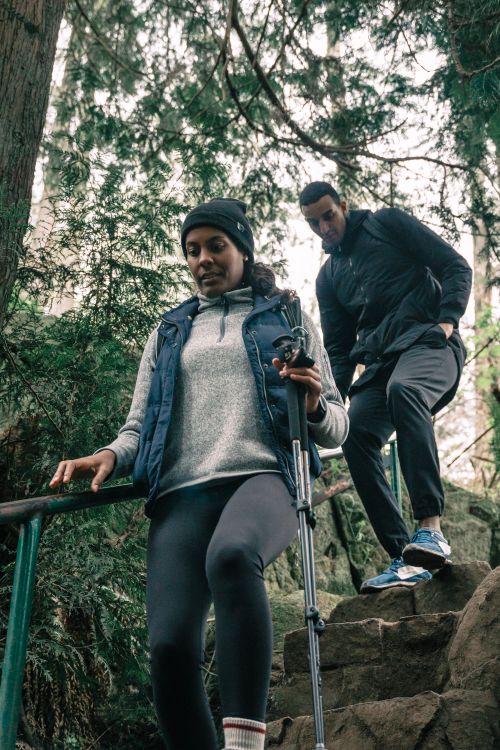 Free A couple descends stone stairs in a dense forest using trekking poles, showcasing outdoor adventure. Stock Photo