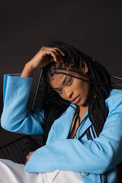 Free Stylish studio portrait of a woman with braided hair, posing in a blue blazer against a dark background. Stock Photo