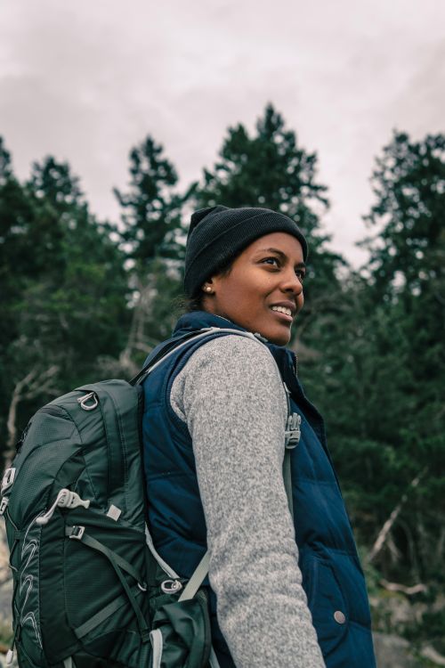 Free Happy woman hiking in nature wearing backpack and beanie, enjoying the outdoors. Stock Photo