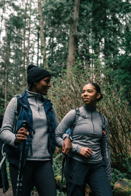 Free Two women hiking and enjoying a conversation in a lush forest trail, showcasing outdoor adventure. Stock Photo