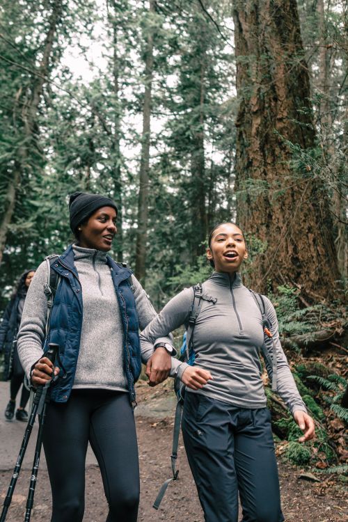 Free Two friends hiking arm in arm through a tranquil forest trail, enjoying nature. Stock Photo