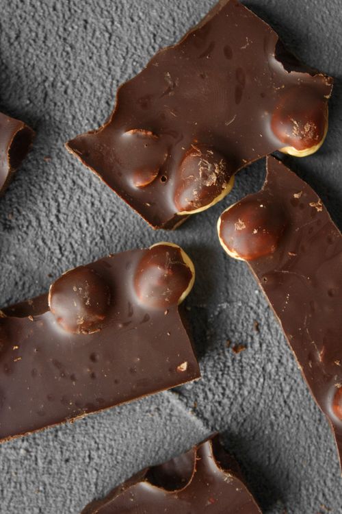 Free Close-up view of dark chocolate pieces with nuts on a grey slate surface, showcasing rich textures and flavors. Stock Photo