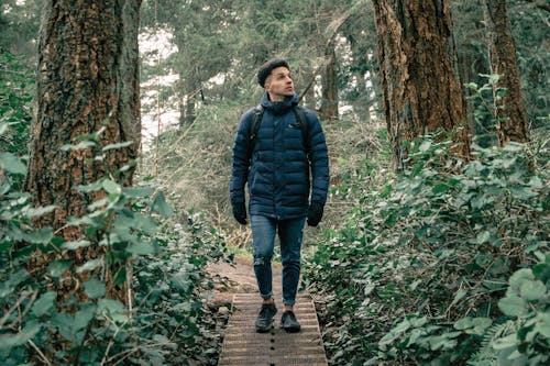 Человек в черной куртке с пузырями стоит на деревянной дорожке посреди леса