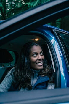 A cheerful woman smiles while sitting inside a car, capturing a joyful outdoor moment.