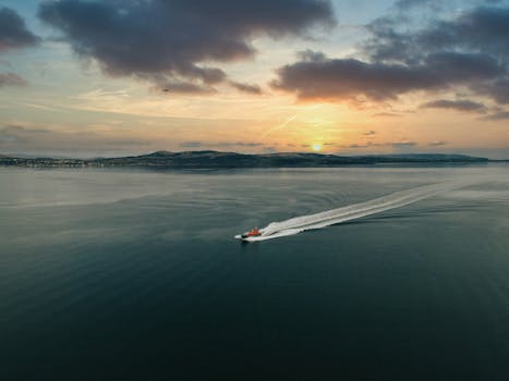 A boat swiftly traverses the serene waters at sunset near Greenock, Scotland, under a dramatic sky.