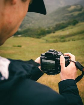 Close-up of a man holding a camera and capturing a scenic outdoor landscape.