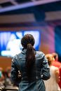 Back view of unrecognizable female viewer with Afro braids enjoying live performance against screen and people