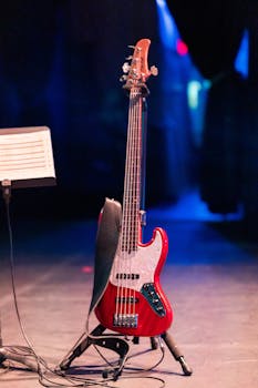 Red electric bass guitar on a stage with a blurred blue background, ready for a performance.
