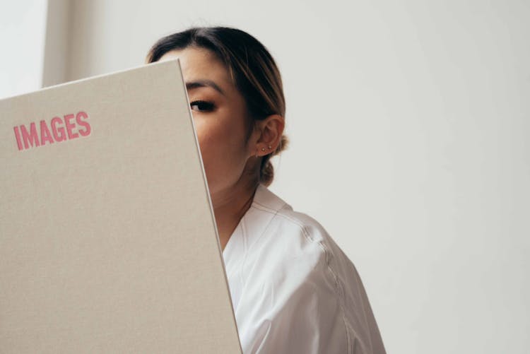 Young Asian Woman Peeking Out From Opened Book