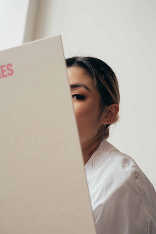 Asian woman covering face with hardcover of book