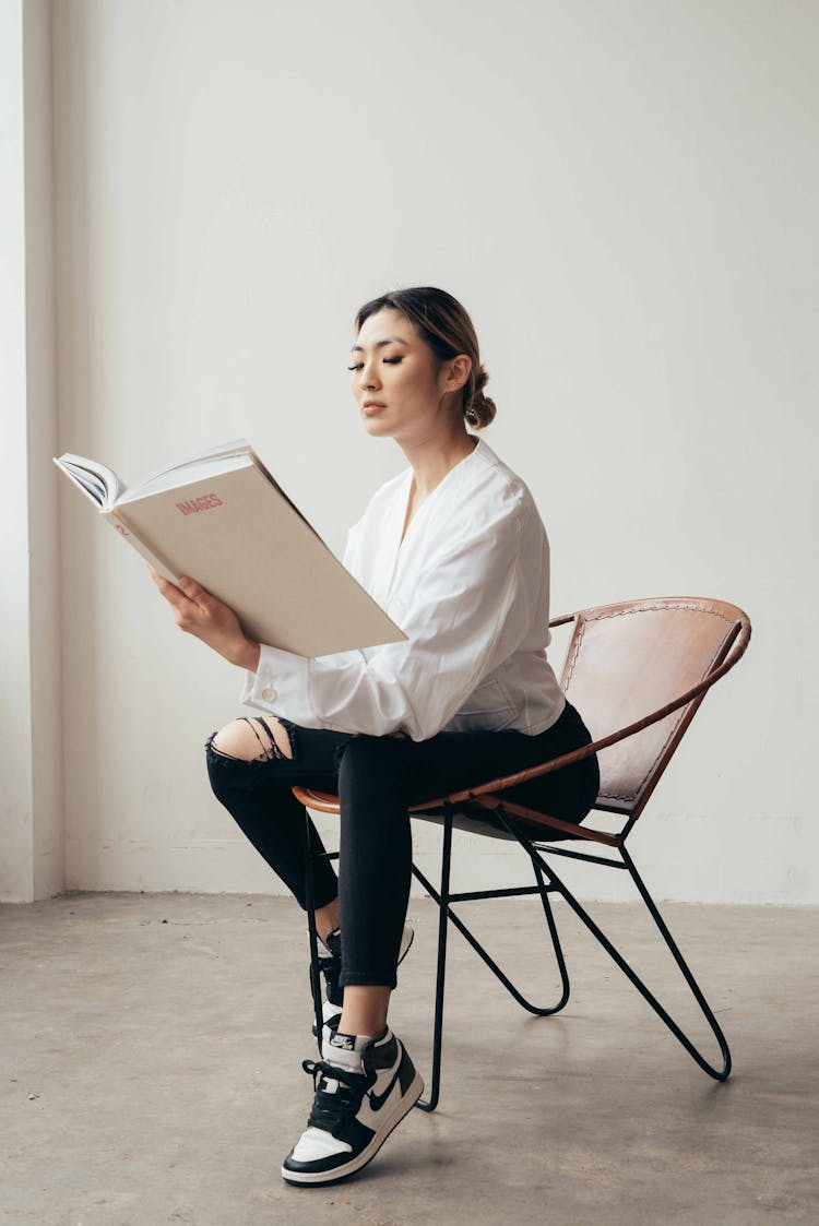 Focused Asian Woman Reading Book In Empty Studio