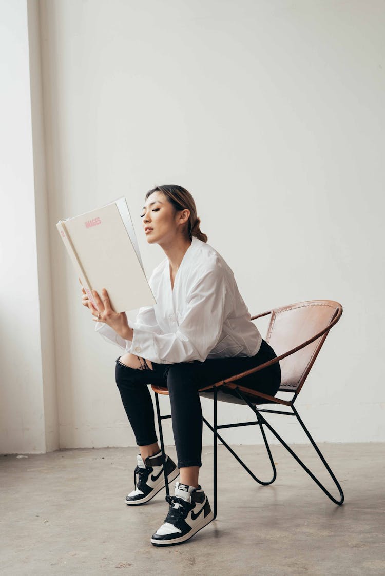 Serious Asian Woman In Armchair Reading Book