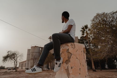 Free A man in casual wear sits on a stone structure outdoors, looking away. Stock Photo