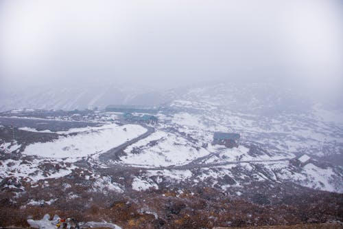 From above of settlement with rustic houses located on snowy area in suburb area in foggy weather on winter day
