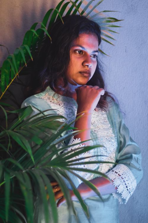 Free Pensive Indian female with black hair in white outfit standing at wall with green plant in light room at home Stock Photo