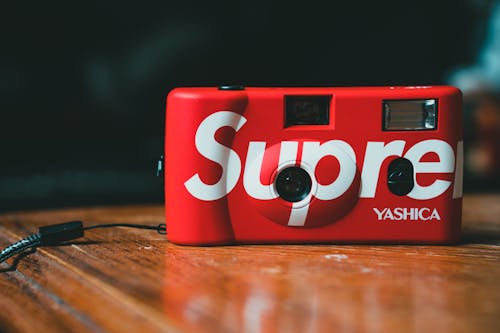 Film red colored photo camera with inscription placed on polish wooden table during charging