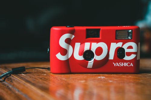 Free Film red colored photo camera with inscription placed on polish wooden table during charging Stock Photo