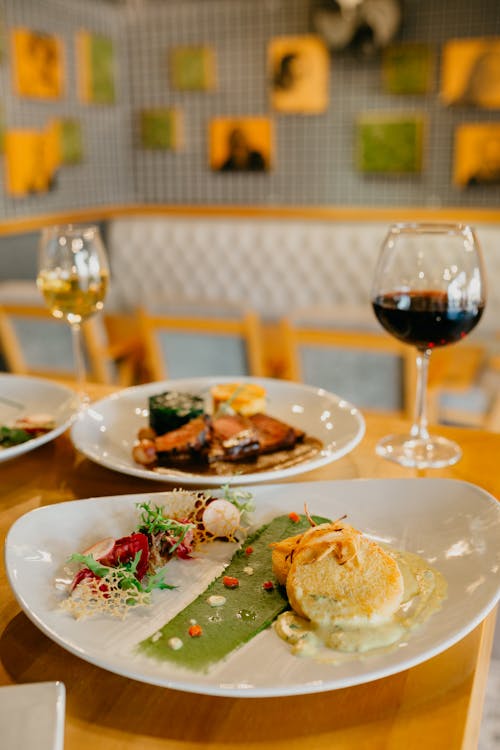 Appetizing delicious dishes on white round plates on wooden table wine glasses of wine in restaurant