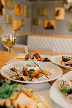 Served table with various delicious dishes and glass of white wine in modern restaurant on blurred background