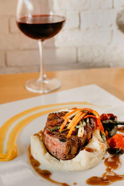 Free From above of appetizing grilled beefsteak with potato puree and vegetables served on wooden table with glass of red wine in restaurant Stock Photo