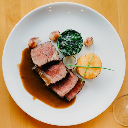 Top view of delicious cut steak garnished with soy sauce and served on table with spinach salad and fried scallop in restaurant