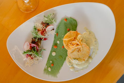 From above of delicious scallops with veggies served on plated decorated with smeared green sauce