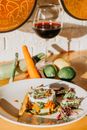 From above of tasty healthy vegetable tart with glass of red wine served on wooden table near raw fresh carrot zucchini and limes in kitchen