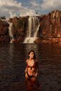 Woman in swimsuit standing in lake against waterfall in daytime
