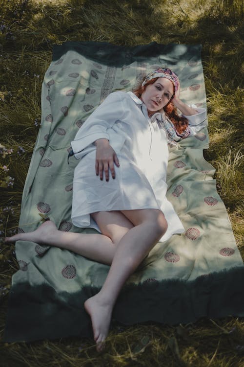 Peaceful young woman lying on blanket on meadow and looking at camera