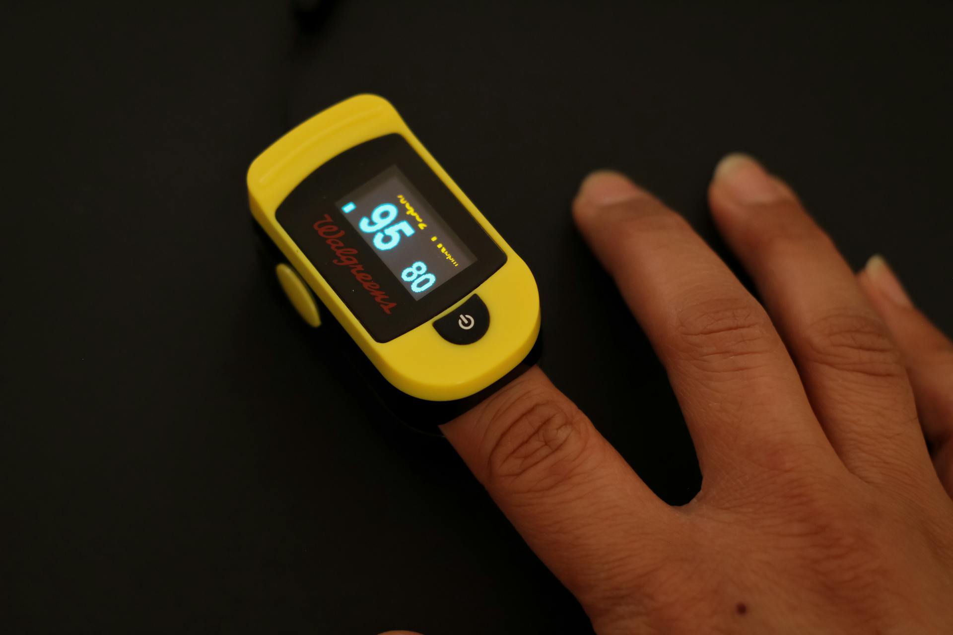 A close-up shot of a yellow pulse oximeter measuring oxygen levels on a finger.