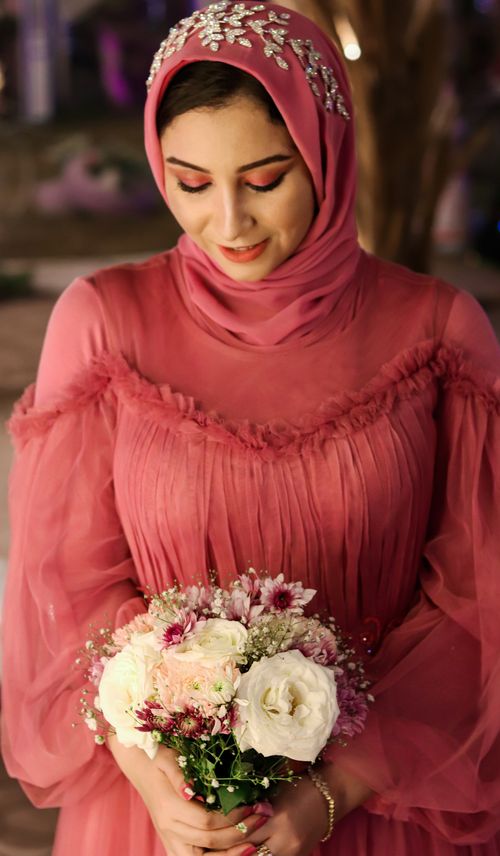 Free A woman in a pink dress holds a bouquet, wearing a decorative hijab in soft evening light. Stock Photo