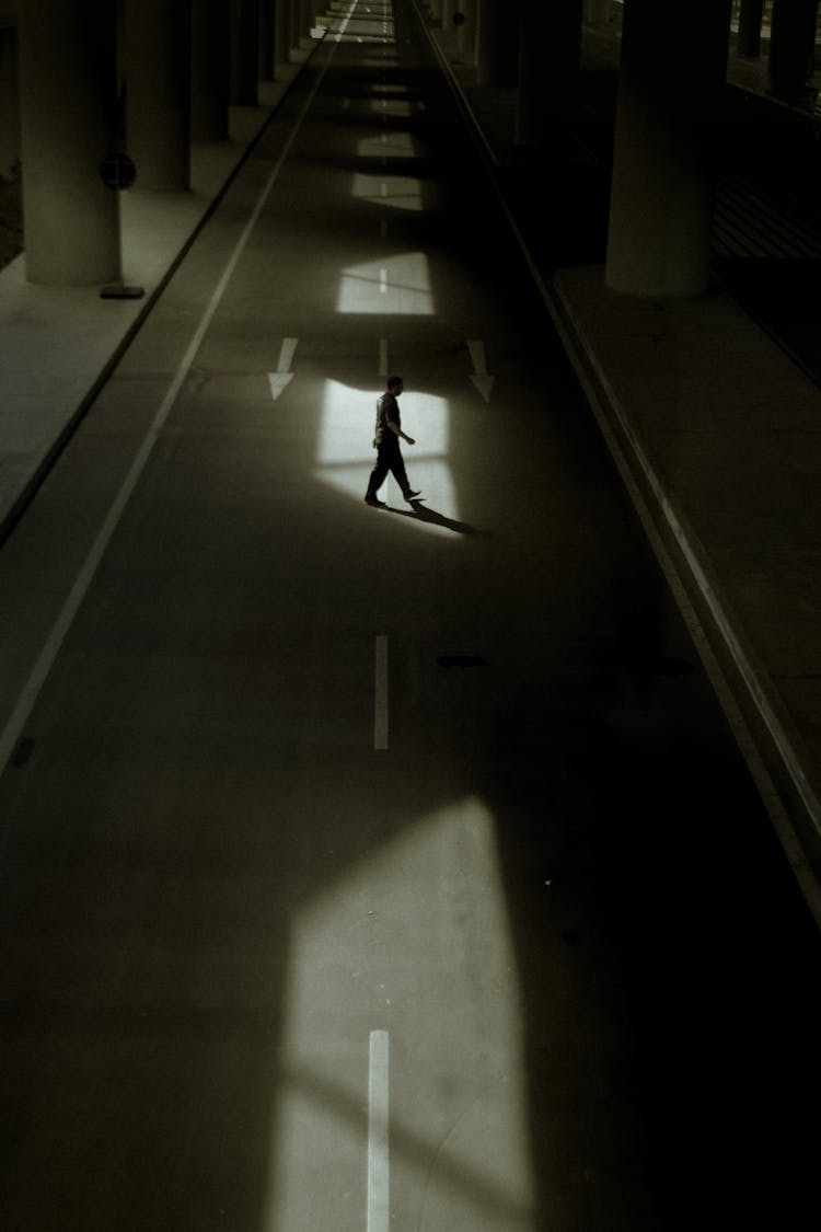 Person Walking On Asphalt Road Under Bridge