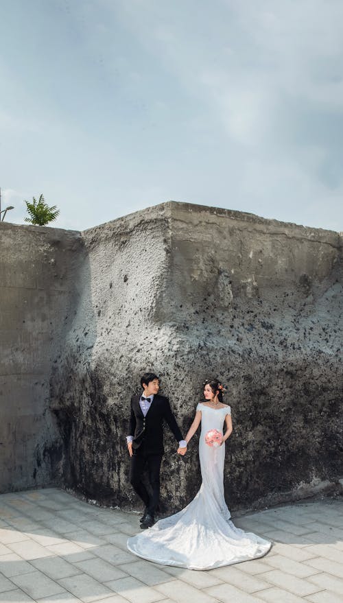 Free A Newlywed Couple Standing in Front of a Concrete Wall Stock Photo