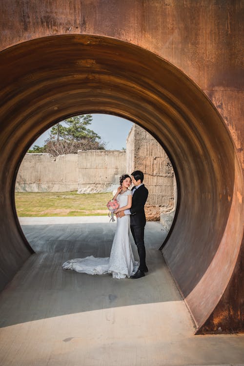 Free A Bride and Groom in Their Wedding Clothes Inside a Tunnel Stock Photo