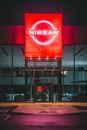 Facade of modern car showroom with glass wall and big shining red signboard in nighttime