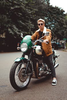 A fashionable man in a brown jacket and sunglasses rides a classic motorcycle on a city street.