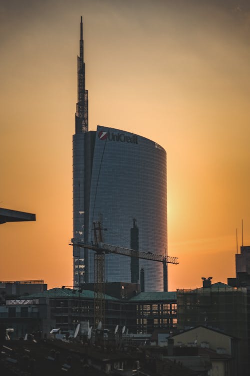 Modern tiled skyscraper under construction with crane located nearby at sunset in city