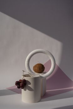 A minimalist composition featuring a coconut and grapes in geometric shapes with soft lighting.