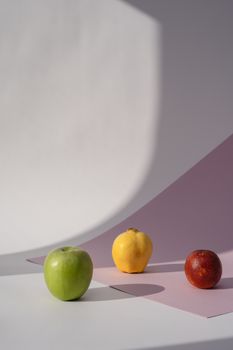 A modern still life composition featuring an apple, quince, and orange against a minimalistic pastel background.