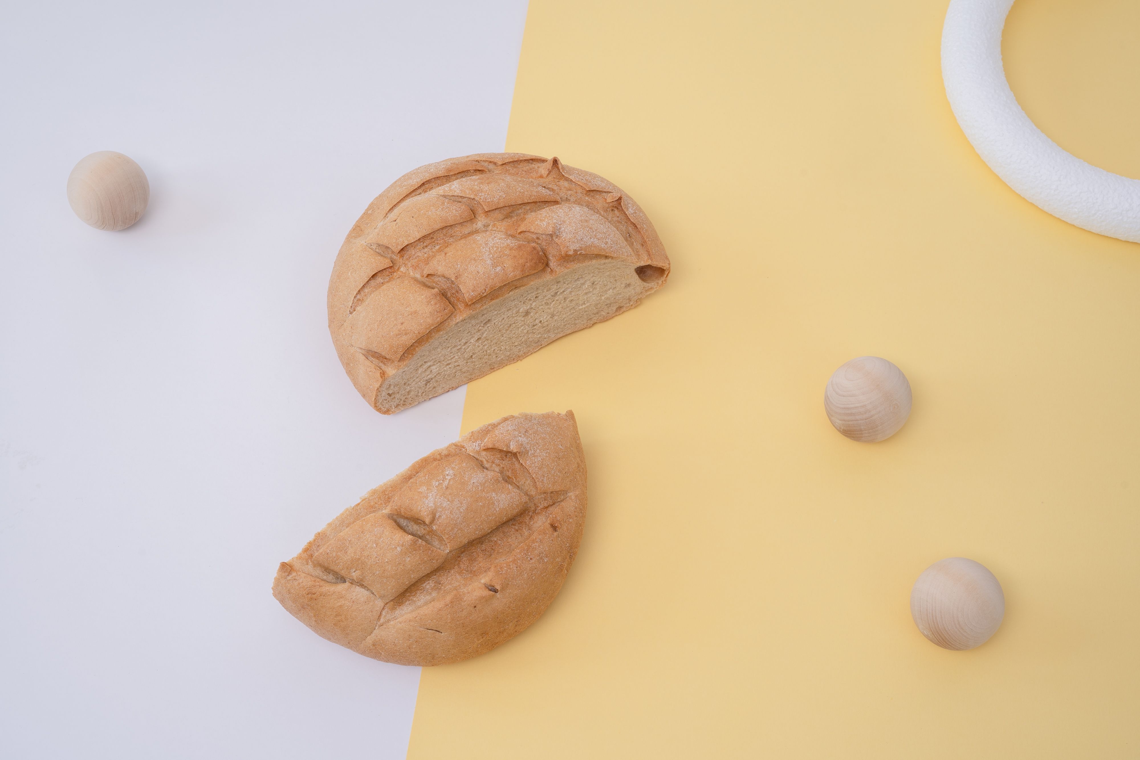 Sliced artisan bread on a dual-tone minimalistic backdrop with wooden spheres.