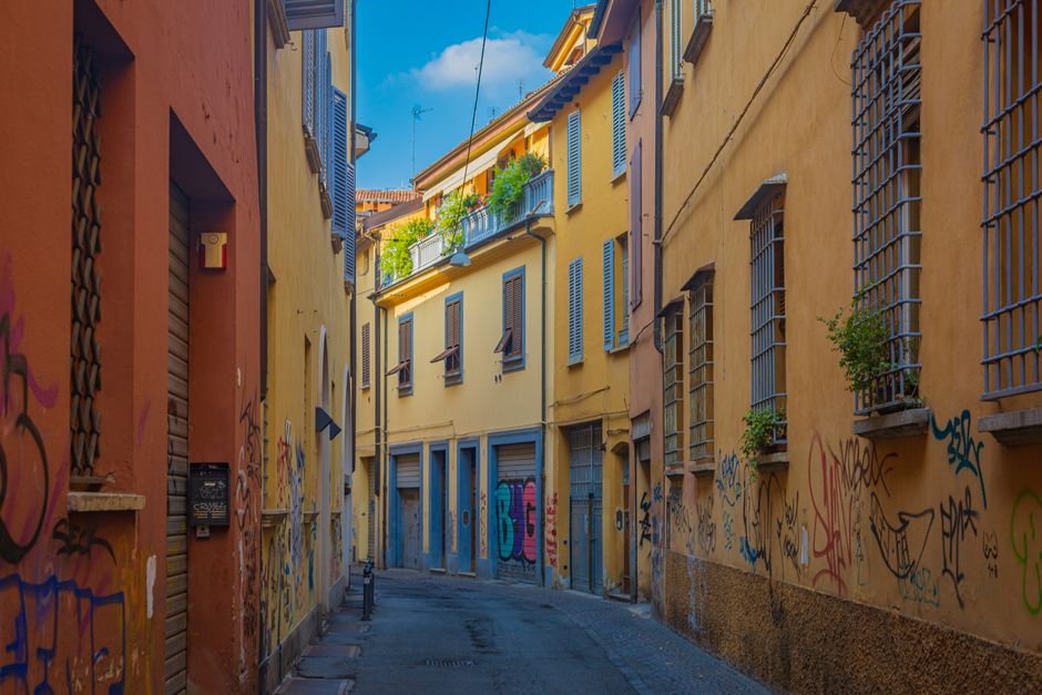 Discover a vibrant alley in Bologna with colorful graffiti and classic Italian architecture.