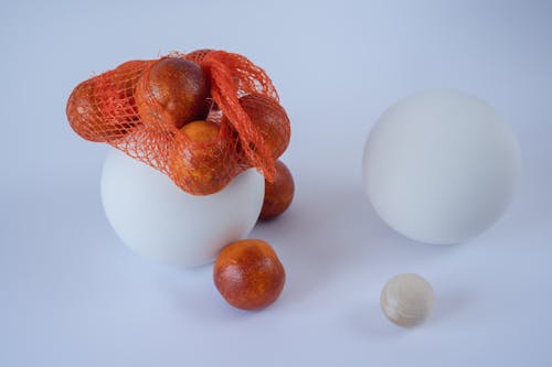 Abstract Composition With Red Oranges in a Net Bag and White Balls