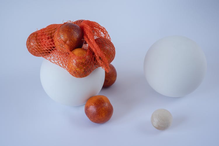 Abstract Composition With Red Oranges In A Net Bag And White Balls