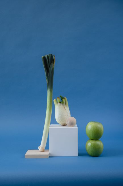 A still life arrangement of vegetables and fruits on geometric shapes with blue background.