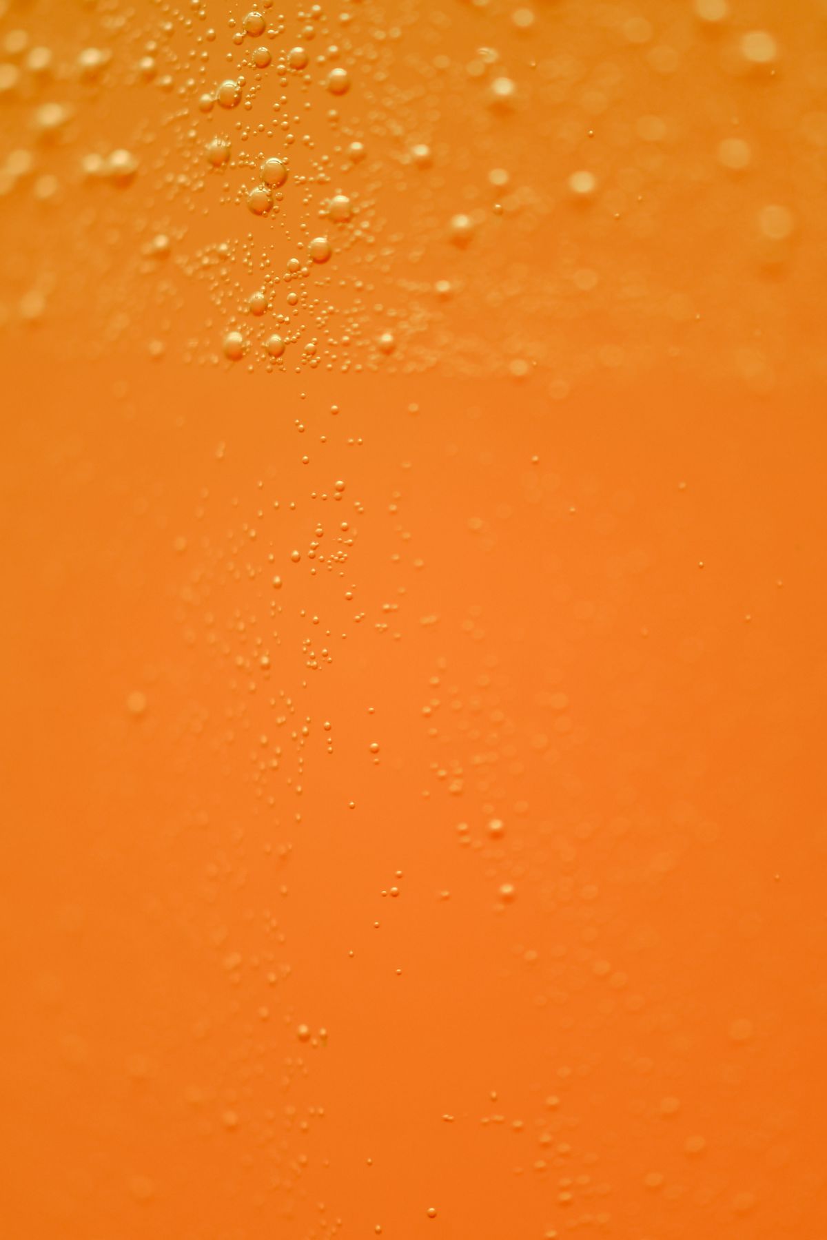 Close-up of carbonation bubbles in a fizzy orange drink, a fast-acting cause of bloating and trapped wind