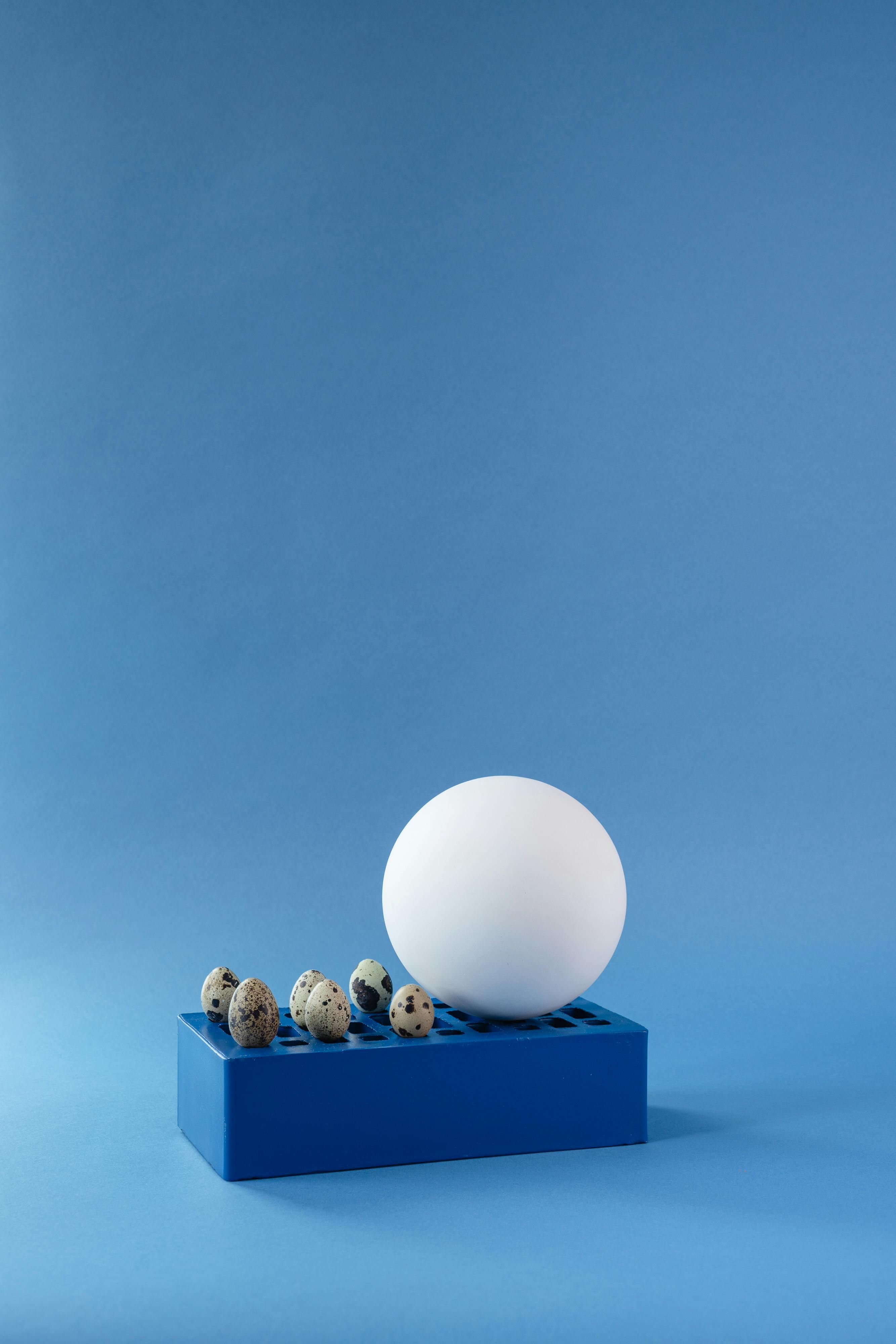 A large white egg and smaller quail eggs on a blue stand against a blue backdrop.