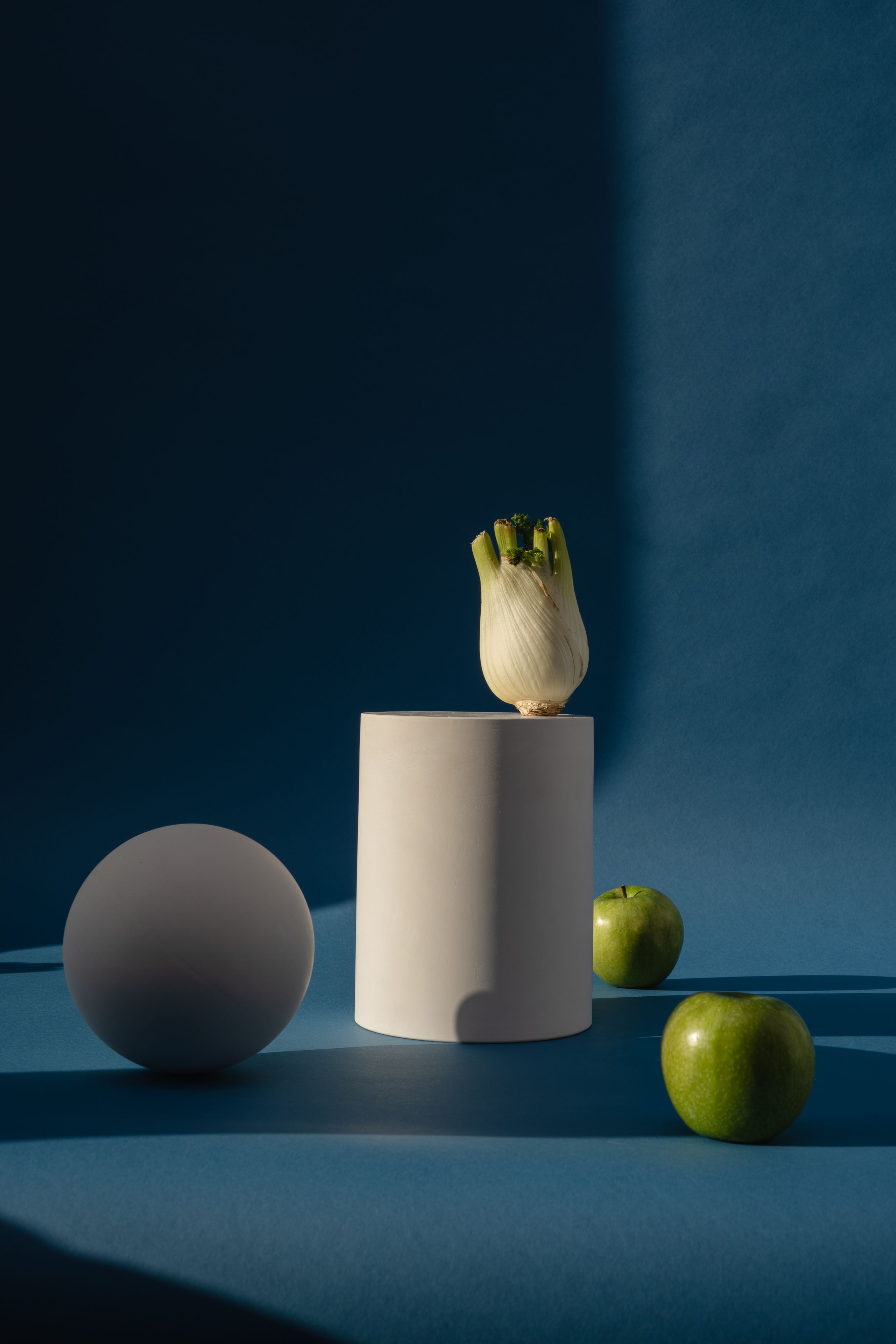 Artistic composition of fennel and green apples on blue background with geometric shapes.