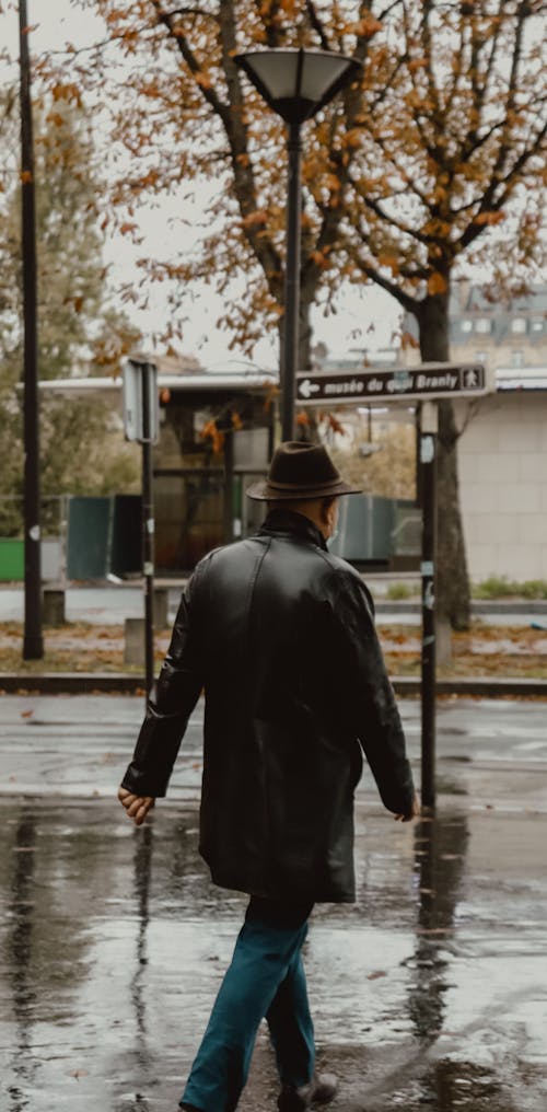 Man in Black Leather Jacket and Black Hat Walking on Sidewalk